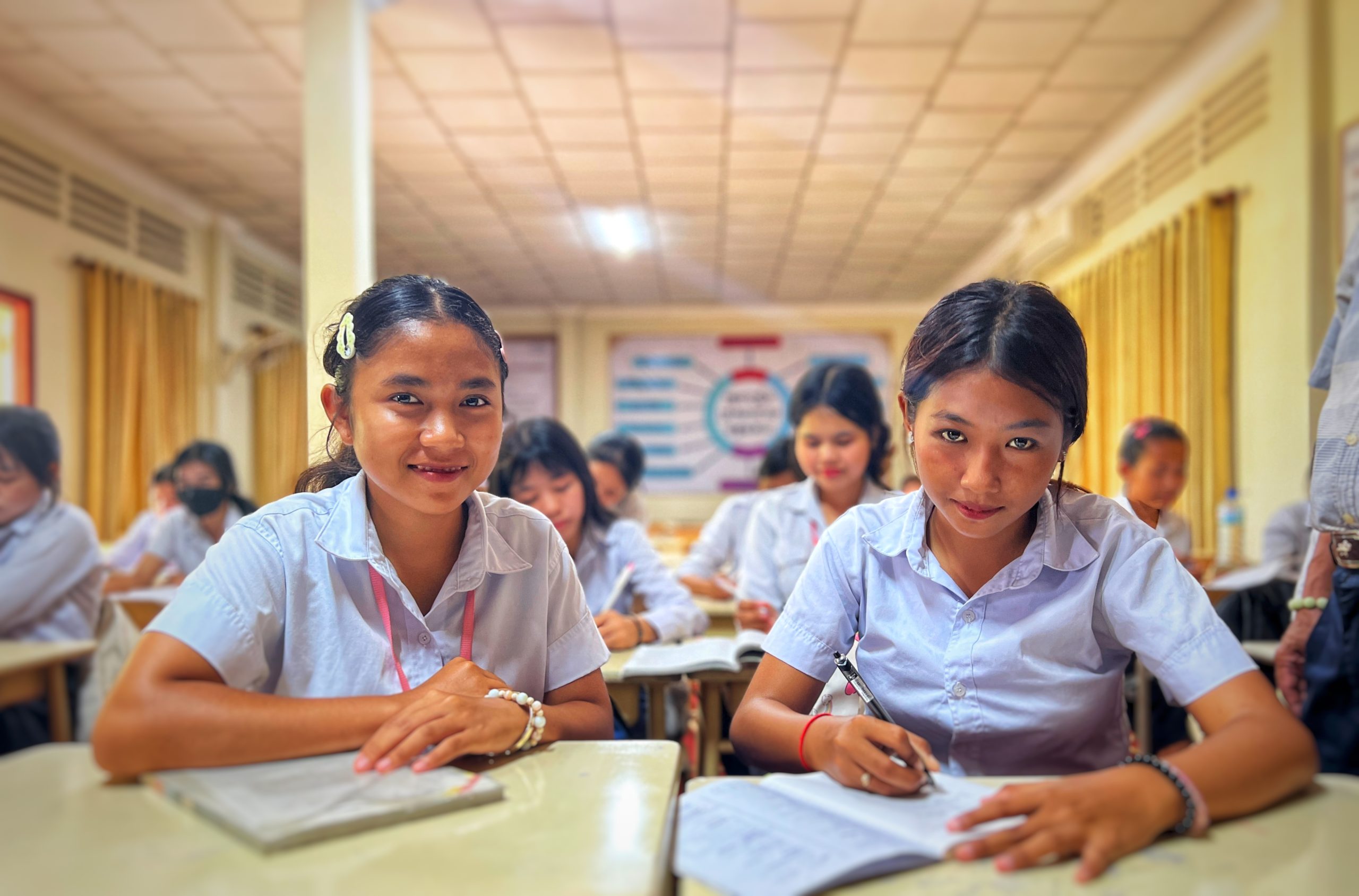 Two Cambodian scholarship students take a break from learning in the classroom to smile at the camera.